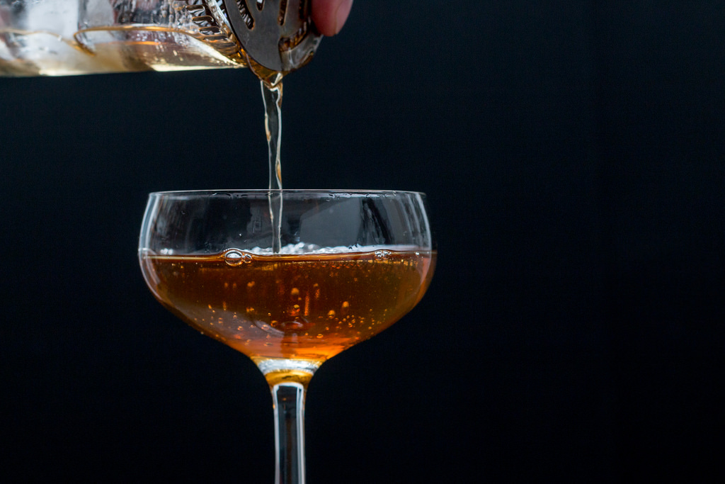 A manhattan being strained from a shaker into a cocktail glass.